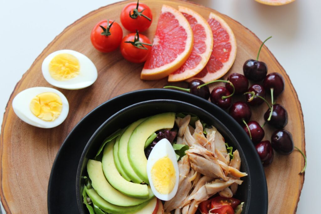 fruit and eggs on a round plate with a bowl of eggs avocados and chicken