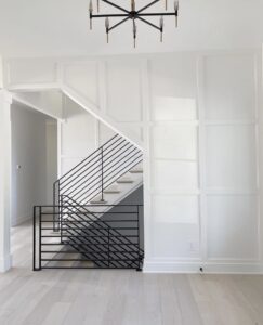 white hallway with black railing on stairs with chandelier