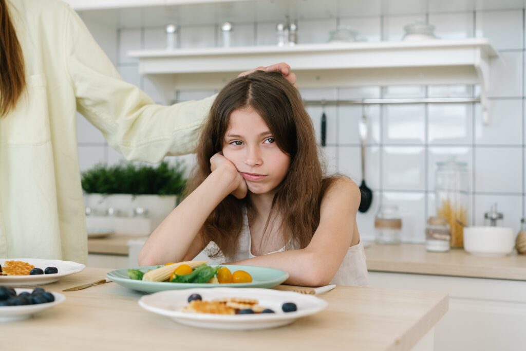 child staring at the camera unhappily with a plate of vegetables